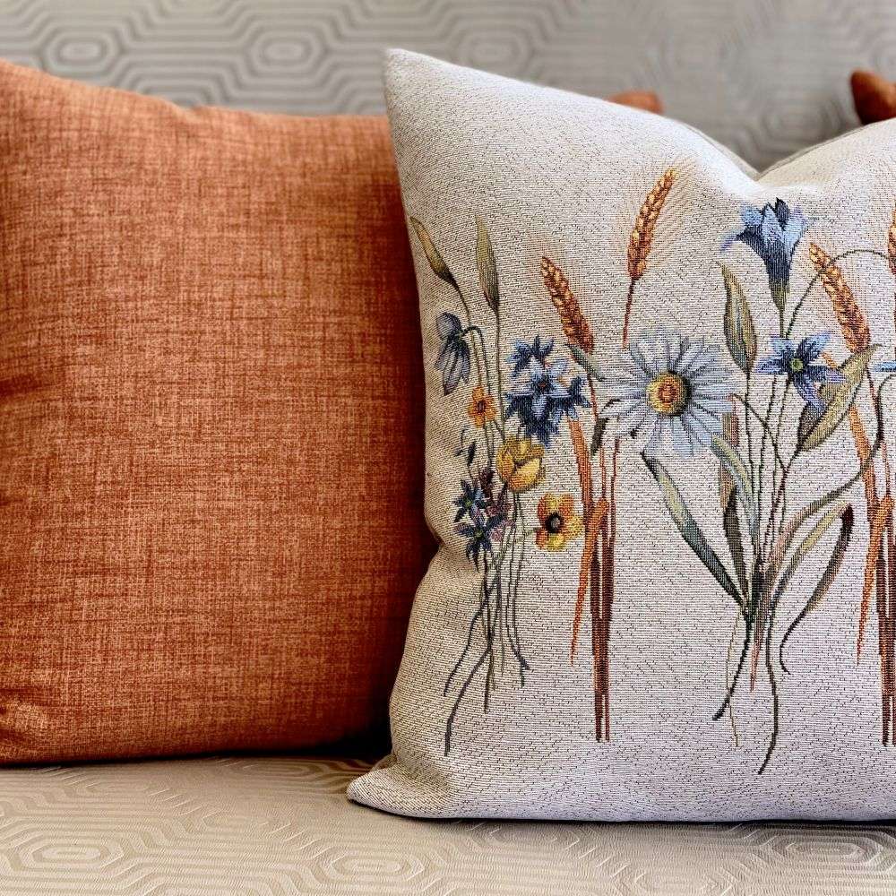 Decorative pillow with floral pattern next to a plain brown pillow on a neutral background