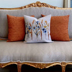 Decorative pillow with floral design on a patterned sofa with orange cushions.