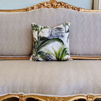 Decorative pillow with palm leaf pattern on a gray sofa with gold trim