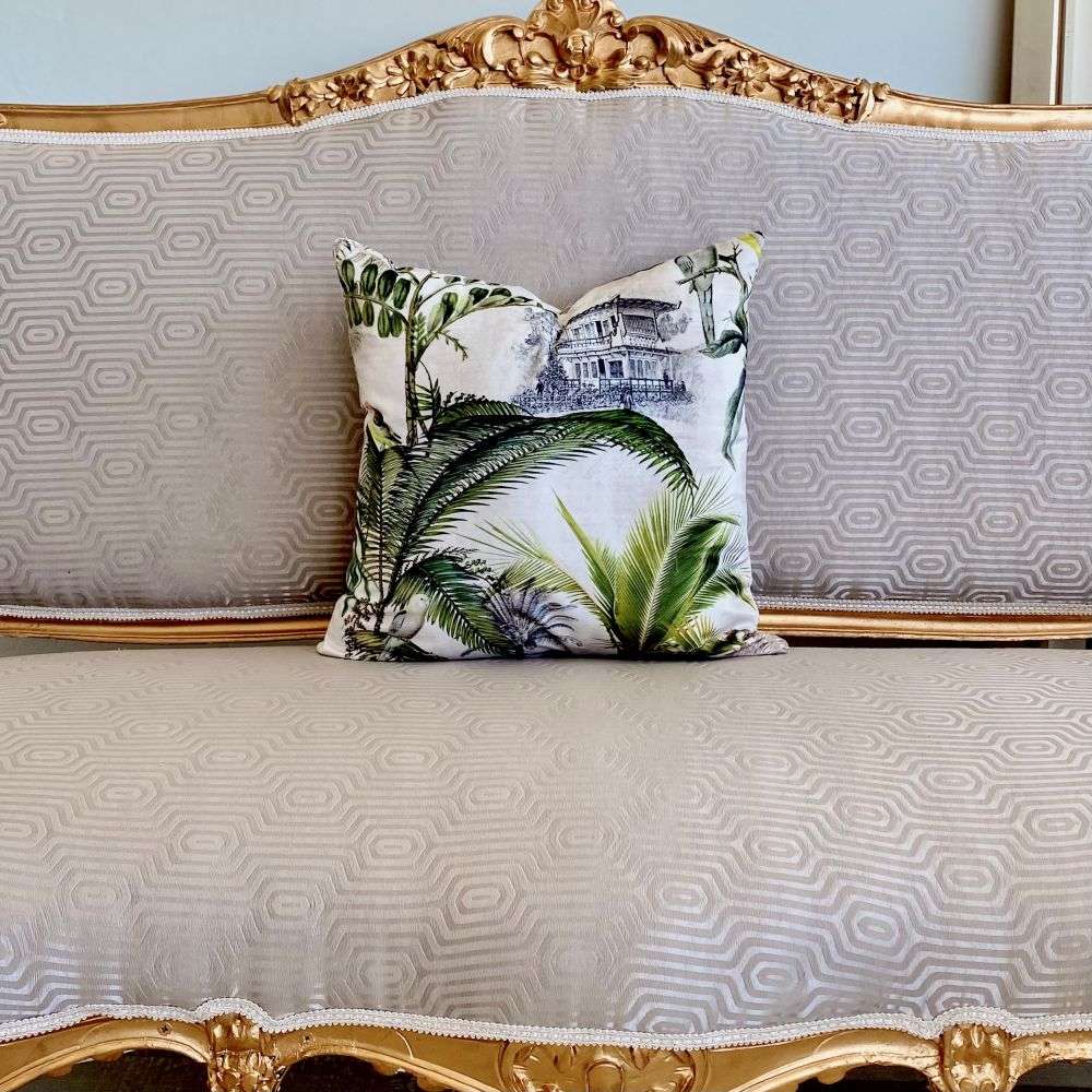 Decorative pillow with palm leaf pattern on a gray sofa with gold trim