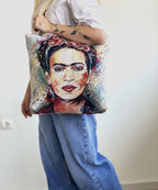 Person holding a tote bag with a Frida Kahlo design against a plain background