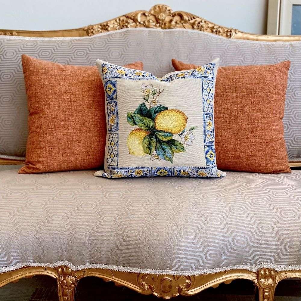 Decorative pillow with lemon design on a patterned sofa with orange cushions.
