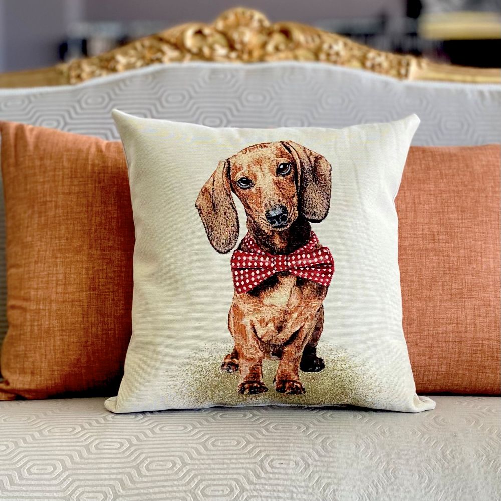 Decorative pillow with a dachshund wearing a red bow tie on a sofa.