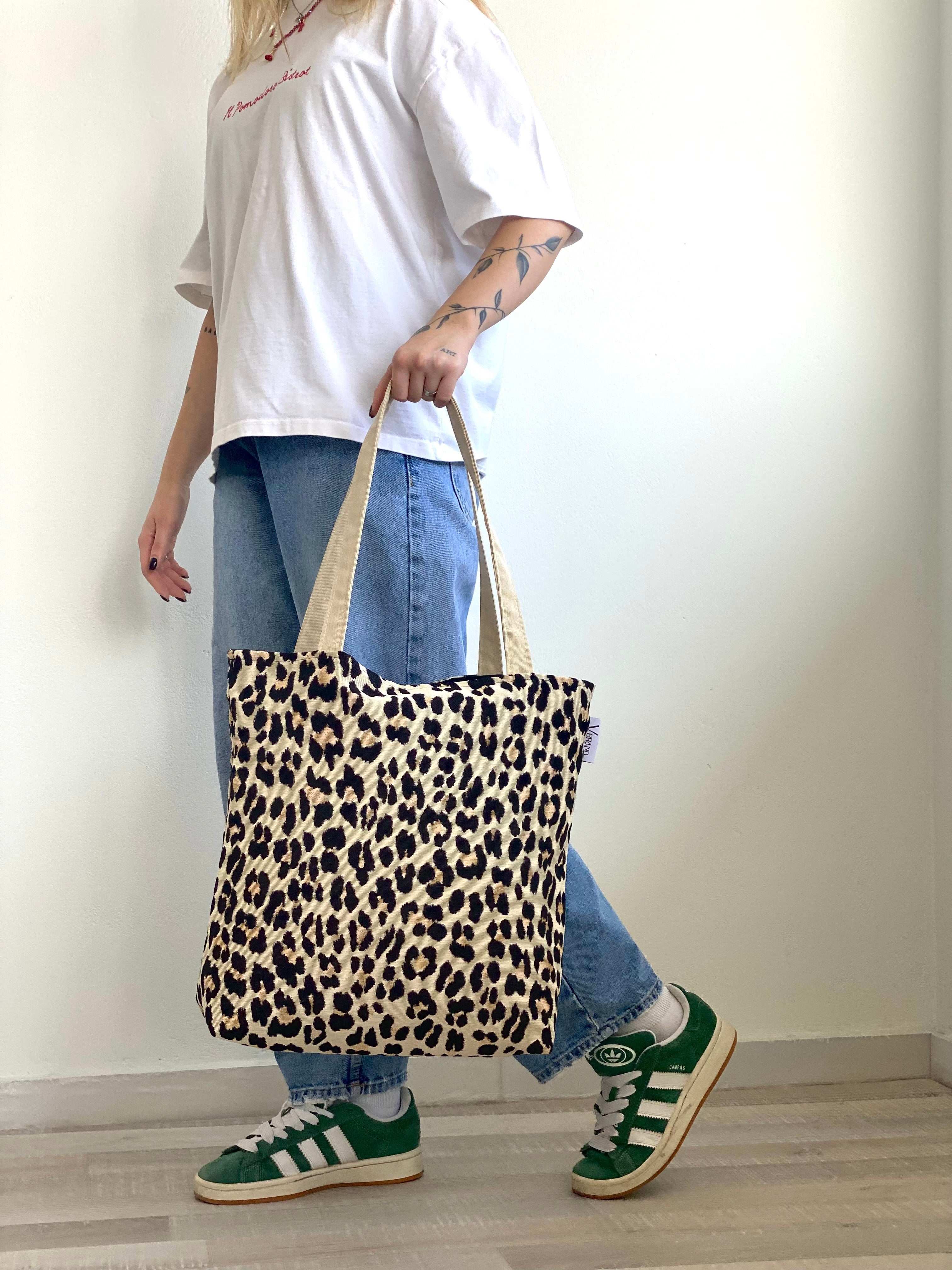 Person holding a leopard print tote bag with a plain background