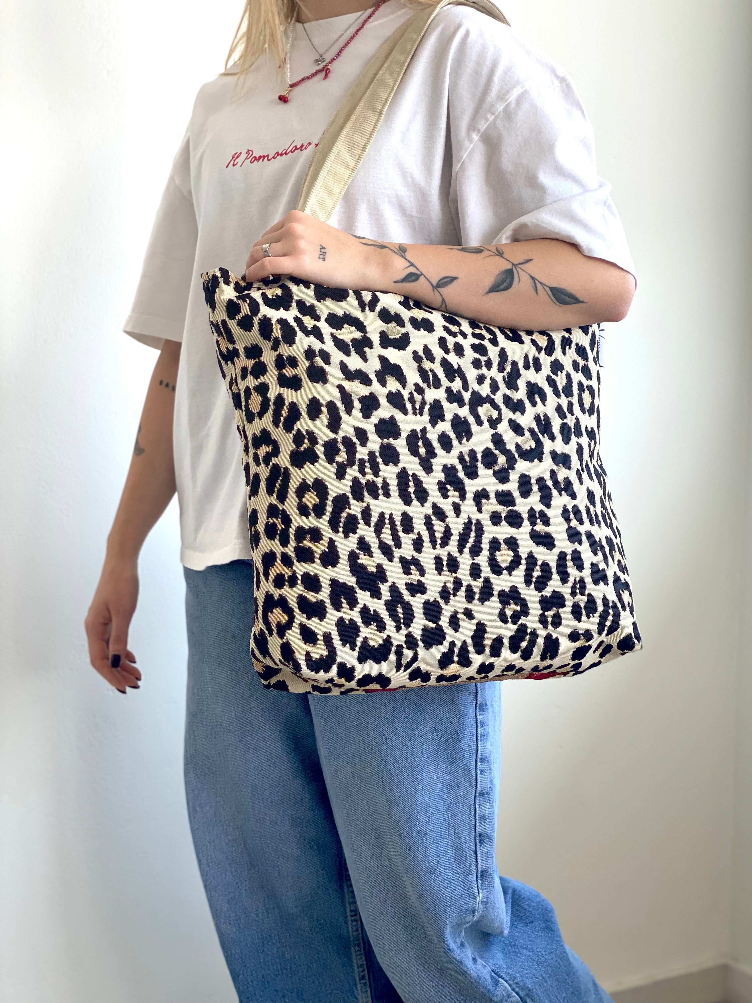 Person holding a leopard print bag against a plain background