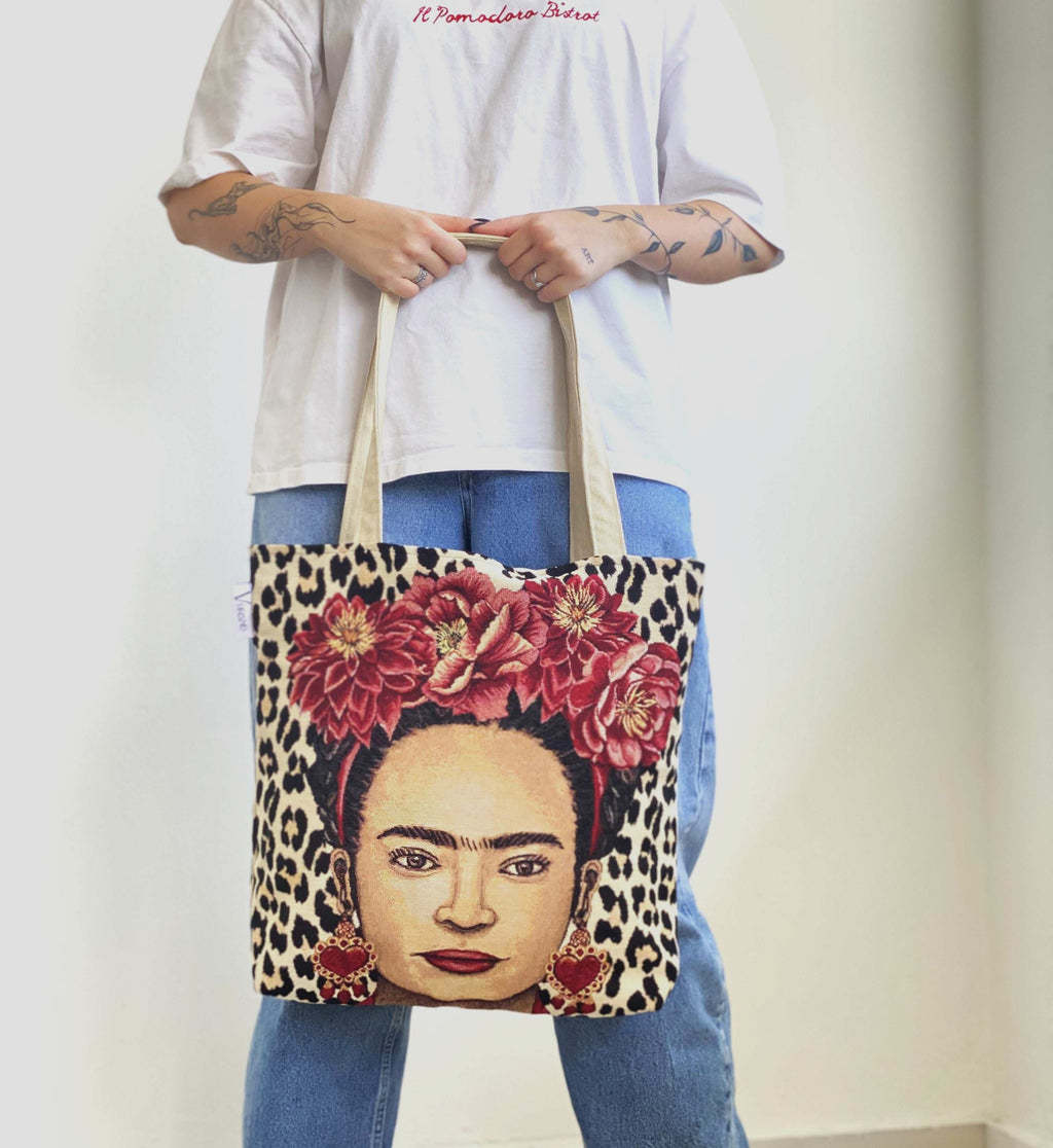 Person holding a tote bag with a design of a woman's face with flowers and leopard print patterns.