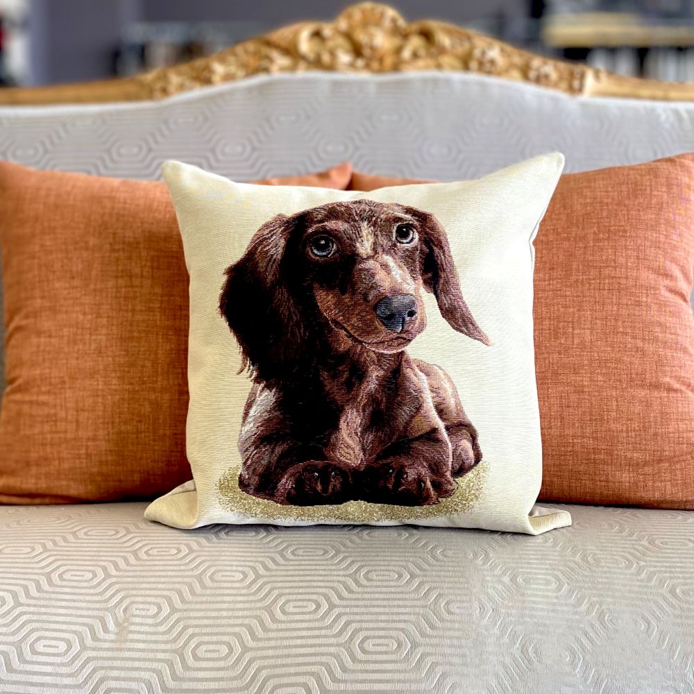 Decorative pillow with a dachshund design on a couch with orange cushions.