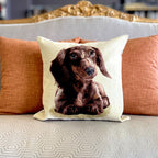 Decorative pillow with a dachshund design on a couch with orange cushions.