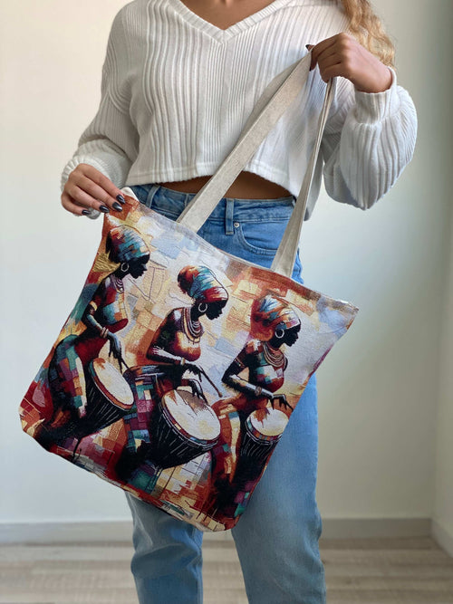 Person holding a tote bag with an artistic design of people playing drums.