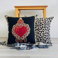 Decorative pillows with a heart design and leopard print on a wooden bench.