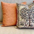 Decorative pillow with tree design next to a plain orange pillow on a textured surface.