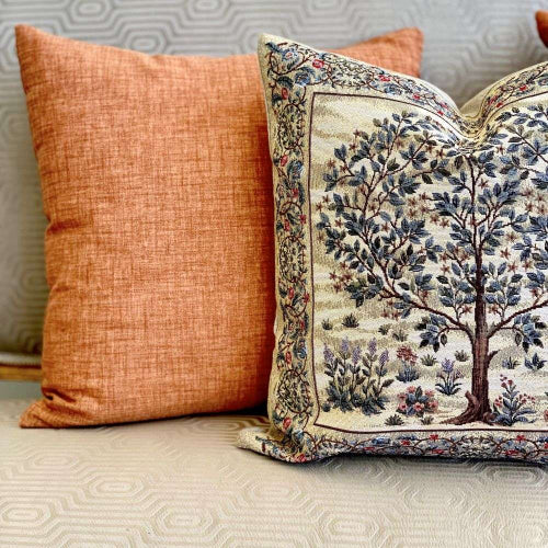 Decorative pillow with tree design next to a plain orange pillow on a textured surface.