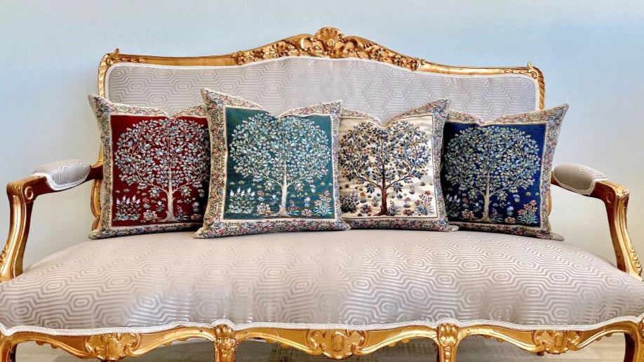 Decorative pillows with tree patterns on a ornate gold and white sofa.