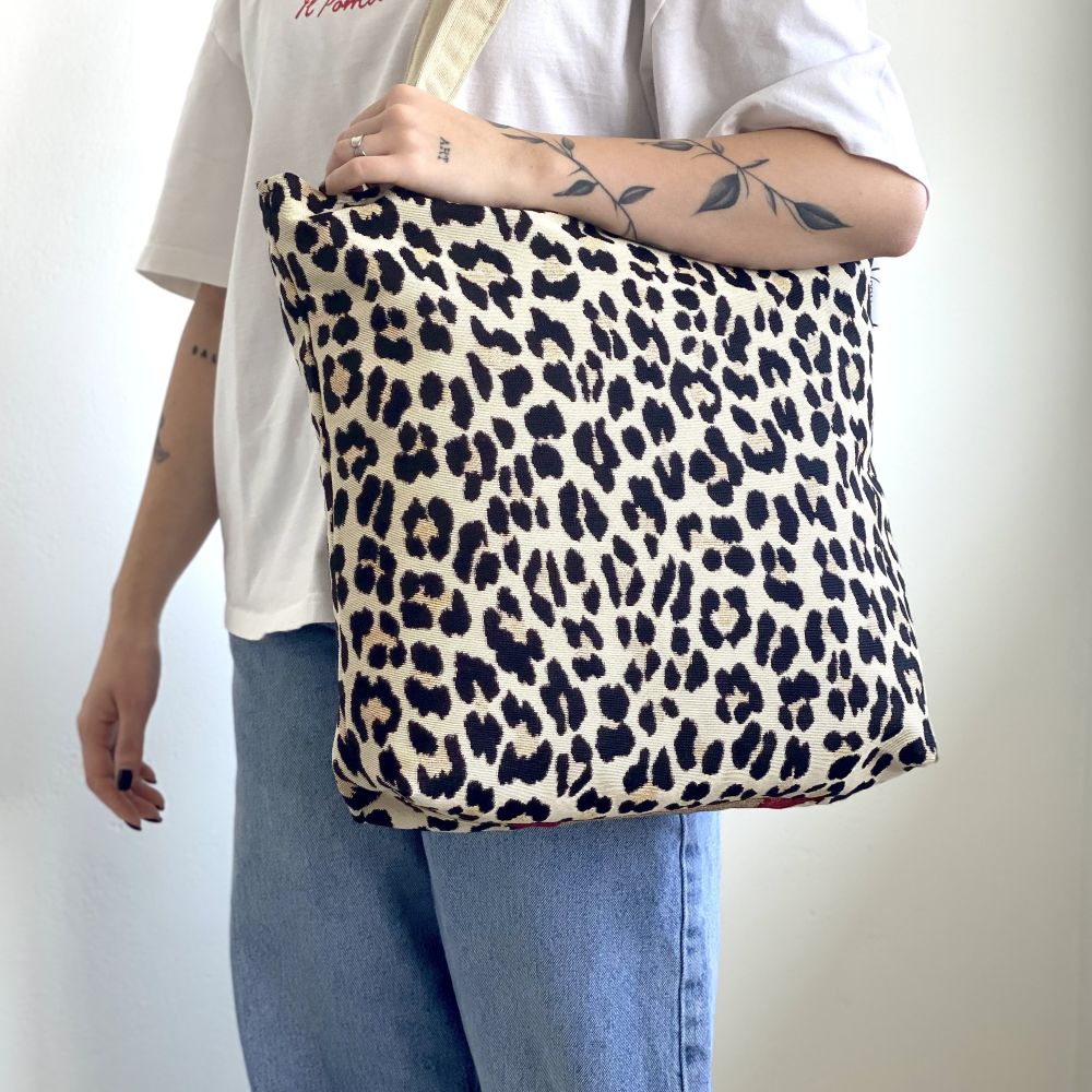 Διακοσμητικά μαξιλάρια με σχέδια ασιατικού θέματος σε έναν καναπέ με σχέδια. Και ένα άτομο που κρατά μια τσάντα με λεοπάρ μοτίβο σε απλό φόντο.