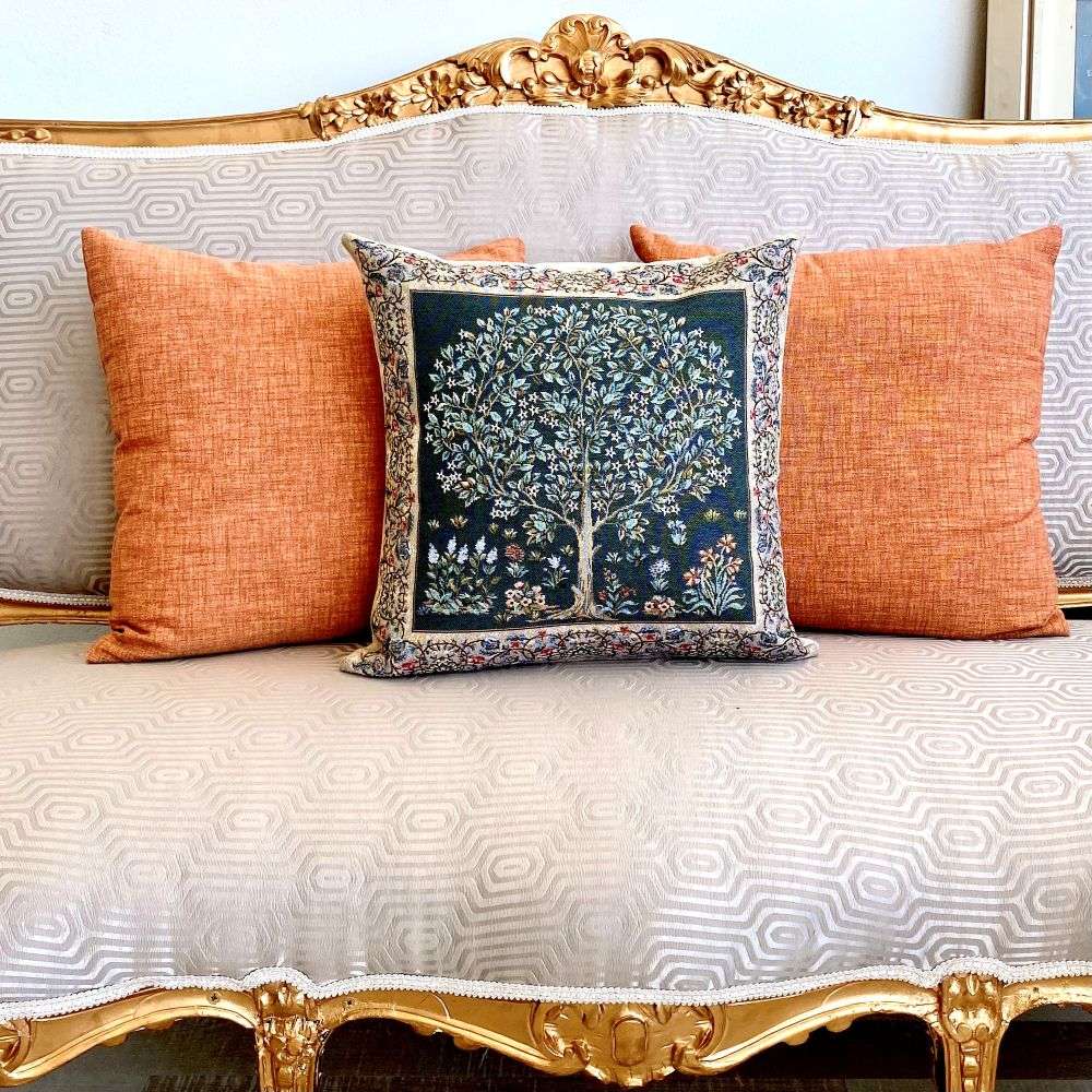 Decorative pillow with a tree design on an ornate sofa with orange cushions.
