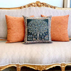 Decorative pillow with a tree design on an ornate sofa with orange cushions.